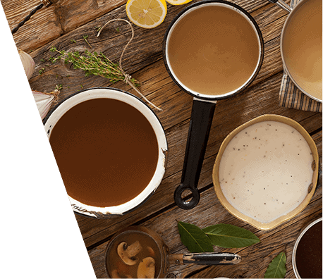 Looking from overhead at a wooden table; on it are pans filled with various brown, peppered and country gravies.