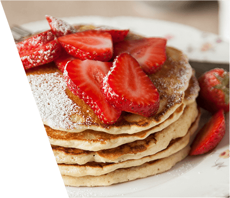 An close up of a stack of pancakes topped with powdered sugar and strawberry slices