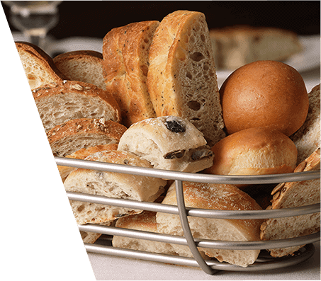 A metal bread basket filled with various artisanal breads and rolls