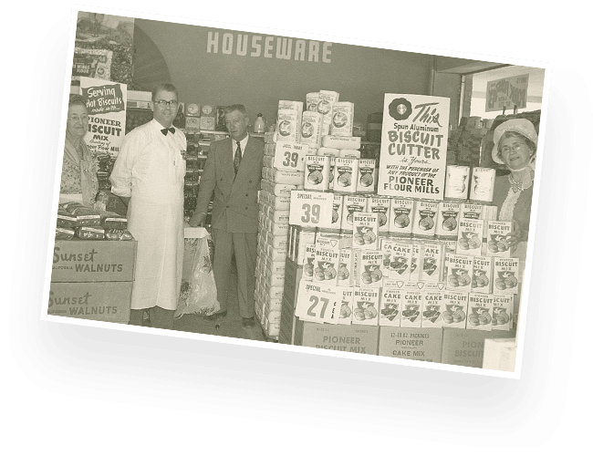 Historical shot of people gathered around a display of Pioneer biscuit mix in a grocery store